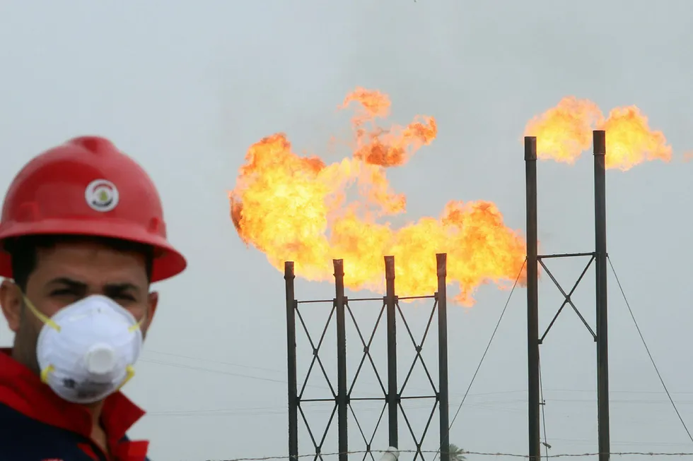 Crisis: flames emerge from flare stacks at Nahr Bin Umar oilfield north of Basra, Iraq as a worker wears a protective mask following an outbreak of coronavirus