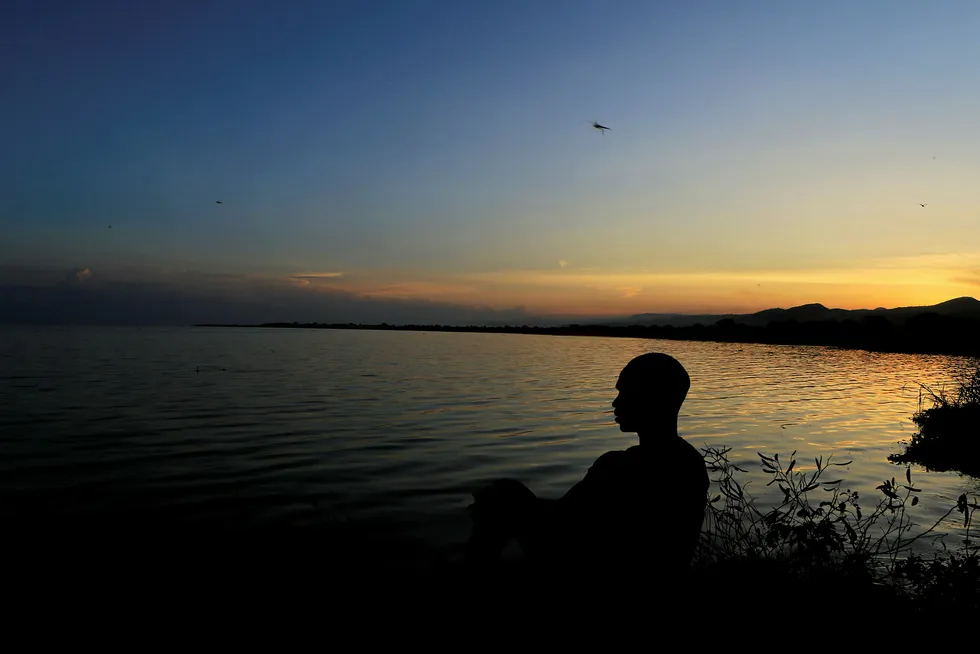 Schedule: a man sits on the shores of Lake Albert at sunset in Panyimur, Uganda