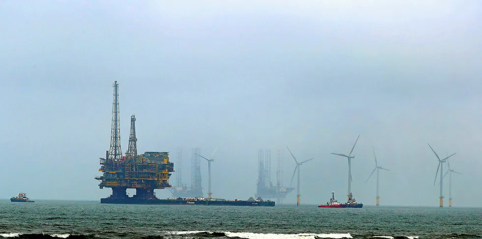 Shell's Brent Delta offshore oil platform being towed in for decommissioning past wind farm along the UK coastline