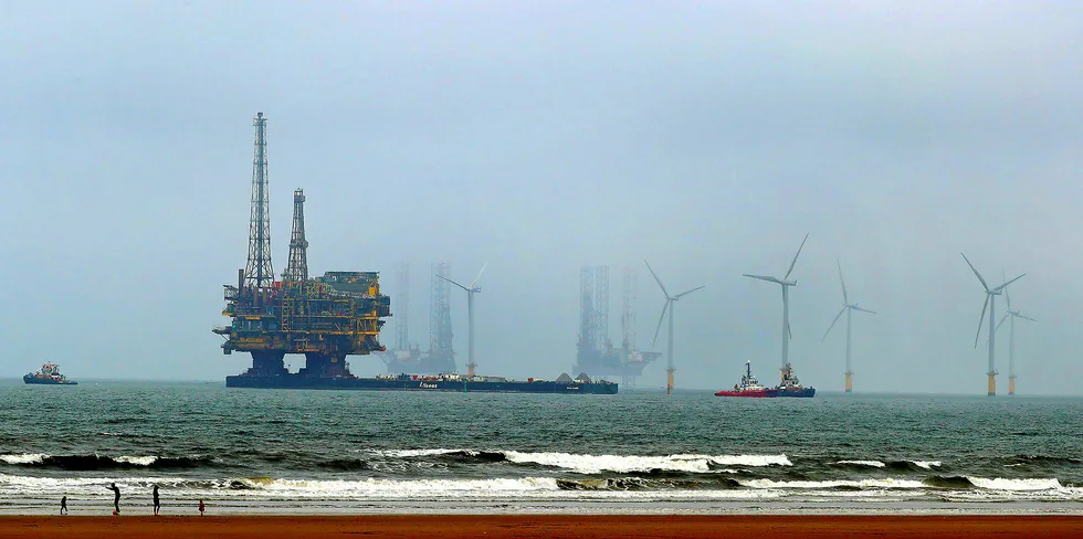 Shell's Brent Delta offshore oil platform is towed past offshore wind turbines off the UK coastline ahead of decommissioning