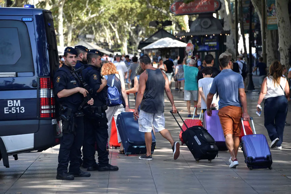 Spanske politimenn står på Rambla Boulevard og passer på mens turister går forbi med koffertene sine, ett døgn etter terroraksjonen som drepte 13 personer og skadde over 100. Foto: PASCAL GUYOT/AFP/NTB scanpix