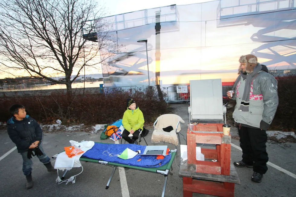 Innleggsforfatter Øystein Krogsrud da han i november sto tre dager ved på brygga i Hamar for å illustrere siktbarrieren fra den planlagte kulverten gjennom strandsonen. På bildet har han besøk av sønnene Suji (fra venstre) og Ravi. Foto: Privat