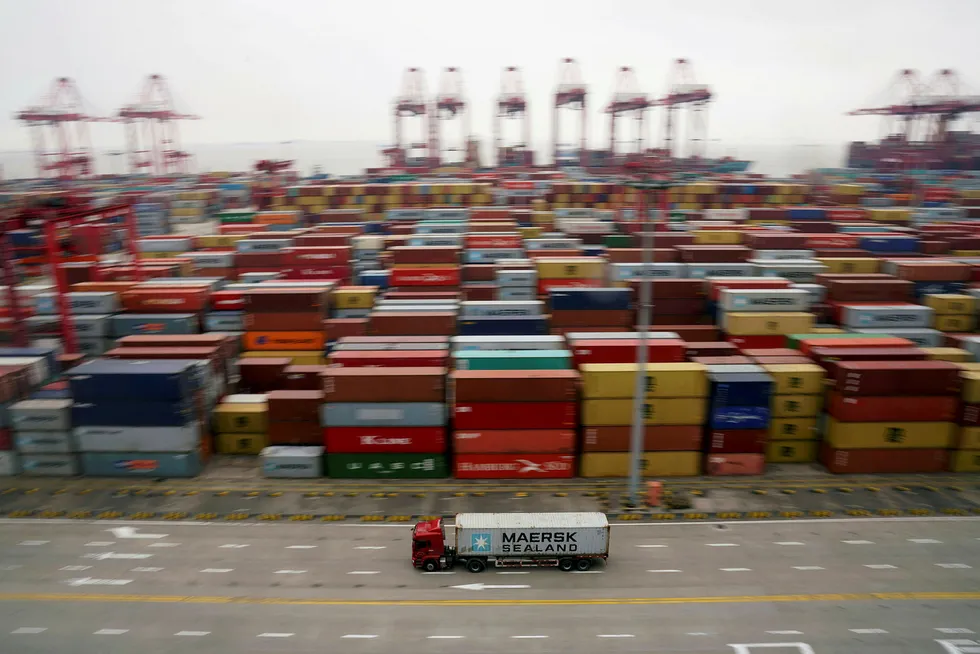 En lastebil kjører forbi containere som ligger ved kaien i Shanghai. Foto: Aly Song/Reuters