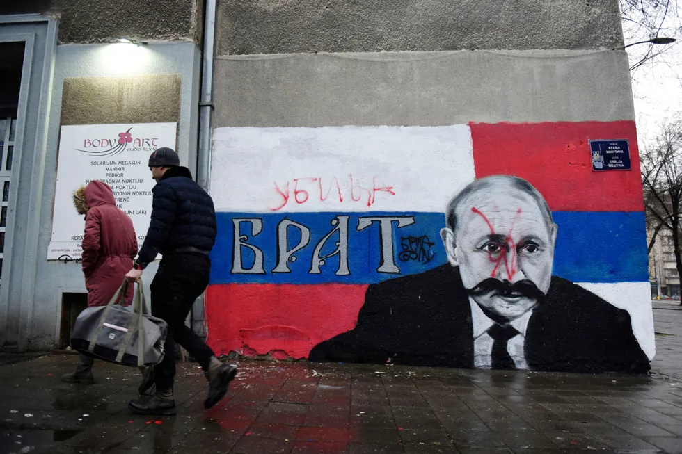 Folk går forbi et veggmaleri i Beograd av Russlands president Vladimir Putin. Veggmaleriet er blitt vandalisert med rød spraymaling og ordet «Morder» skrevet over originalteksten som lyder: «Bror».
