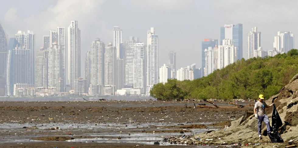 A volunteer carries a plastic bag as he collects garbage, with the skyline of Panama city in the background, during the National Beach Clean-up day