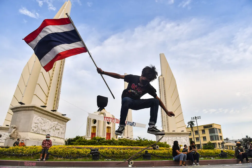 A protester: holds the Thai national flag while riding a skateboard at Democracy Monument in Bangkok
