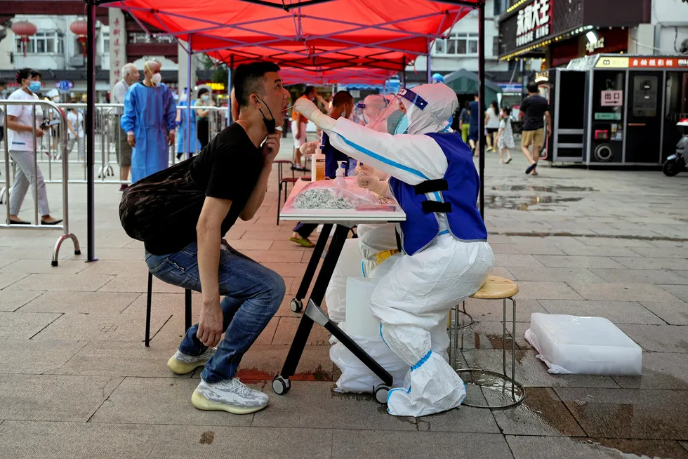 Feeling the heat: a medical worker, wearing a protective suit and sitting with an ice block between the legs, collects a swab from a resident at Covid testing site amid a heatwave warning in Shanghai last week