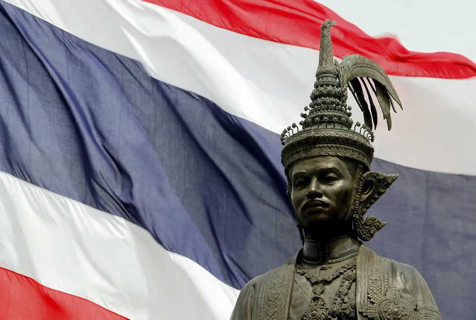 Flagging: Thai national flag waves in the wind behind a statue of King Rama VII in front of the parliament building in Bangkok