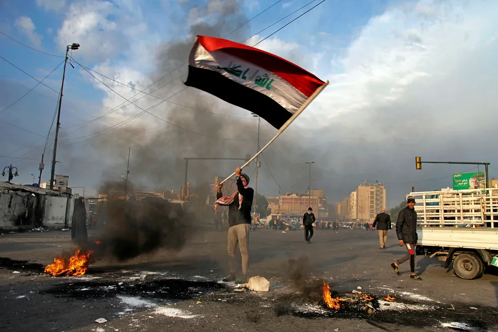 Iraq Oil: a protester waves an Iraqi flag while demonstrators set fire to close streets near Tahrir Square