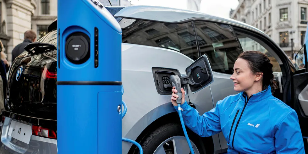 A BMW staff member poses for a photograph as she connects a BMW i3 electric vehicle to a charging point.