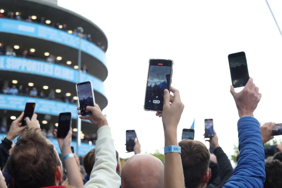 Hva gjør det med oss at vi ser verden gjennom mobilen, og følger spillereglene den dikterer? Bildet viser fans som strekker seg for å ta bilde av spillerne på vei inn før forrige Manchester-derby på Etihad.