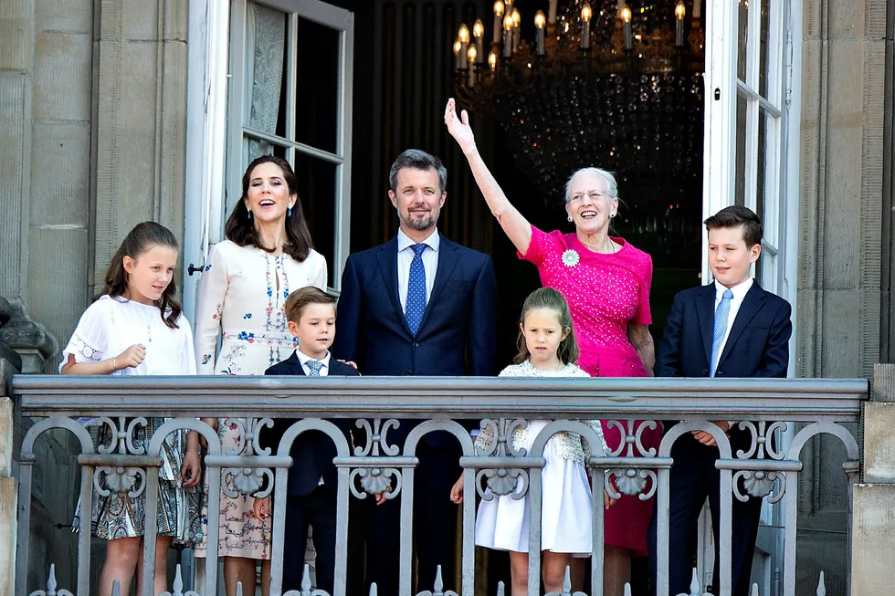 Danmarks kongelige familie, med Dronning Margrethe i rosa, vinker fra balkongen på Amalienborg Slot.