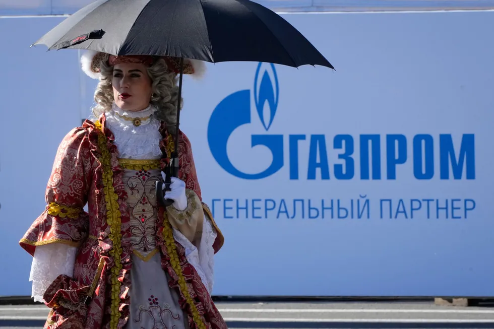 Shade: an actor wearing an 18th Century costme walks past a Gazprom logo in St Petersburg, Russia