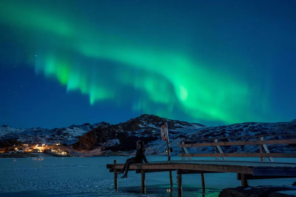 Mesmerising lights: A person sits on a pier watching Northern Lights on an island in Norway