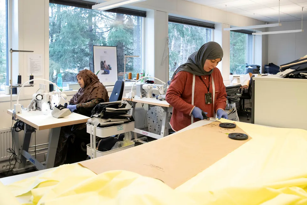Hodan Jama Farrah (i bakgrunnen) syr og Fatima Malala klipper til bomullsstoff til en smittervernsfrakk på bedriften Sisters in Business i Asker. Sisters in Business er et sosialt entreprenørskap som rekrutterer og sysselsetter innvandrerkvinner.