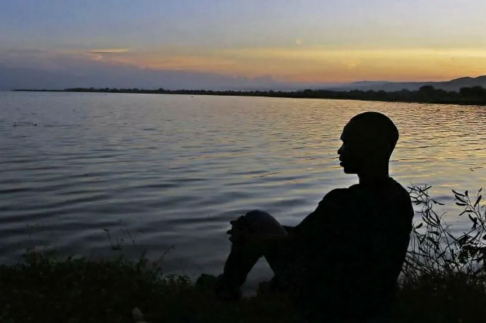 View: a man watches the sunset from the shores of Lake Albert, Uganda