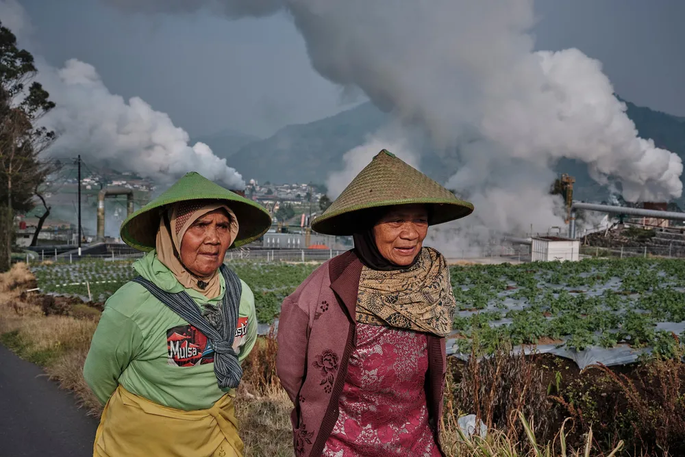 Farmers walk by as steam rises from a geothermal power plant in Dieng, Central Java, Indonesia.