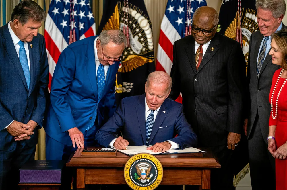 US President Joe Biden signs the Inflation Reduction Act of 2022 into law at the White House on August 16, watched by key lawmakers including the bill's authors, Senator Joe Manchin, left, and Senate Majority Leader Chuck Schumer, second left.