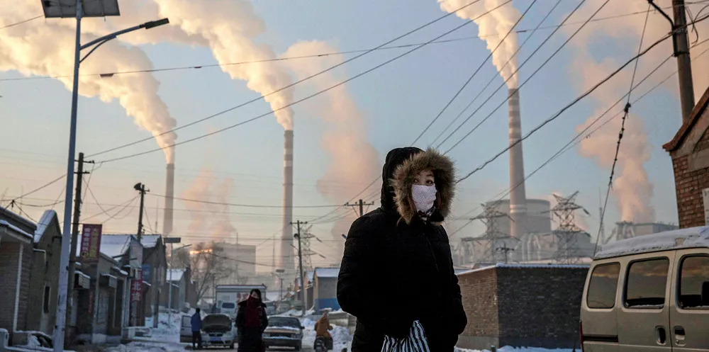 Smoke billows from stacks as a Chinese woman wears as mask while walking in a neighborhood next to a coal fired power plant in Shanxi, China.