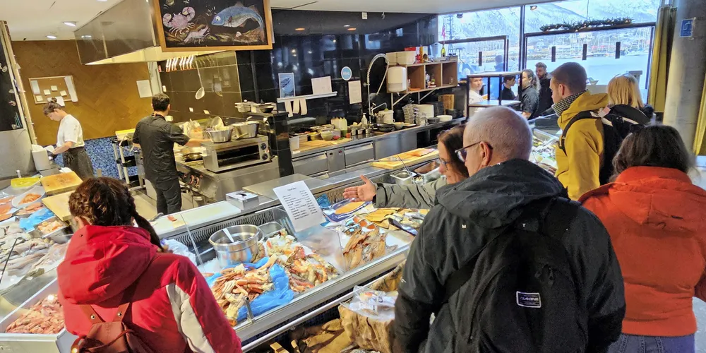 Turister flokker seg rundt sjømatdisken til fiskebutikken Dragøy på Kysten hus i Tromsø onsdag 6. mars 2024. Sjømatrådets direktør vil at nordmenn skal være like begeistret for norsk sjømat som turistene.