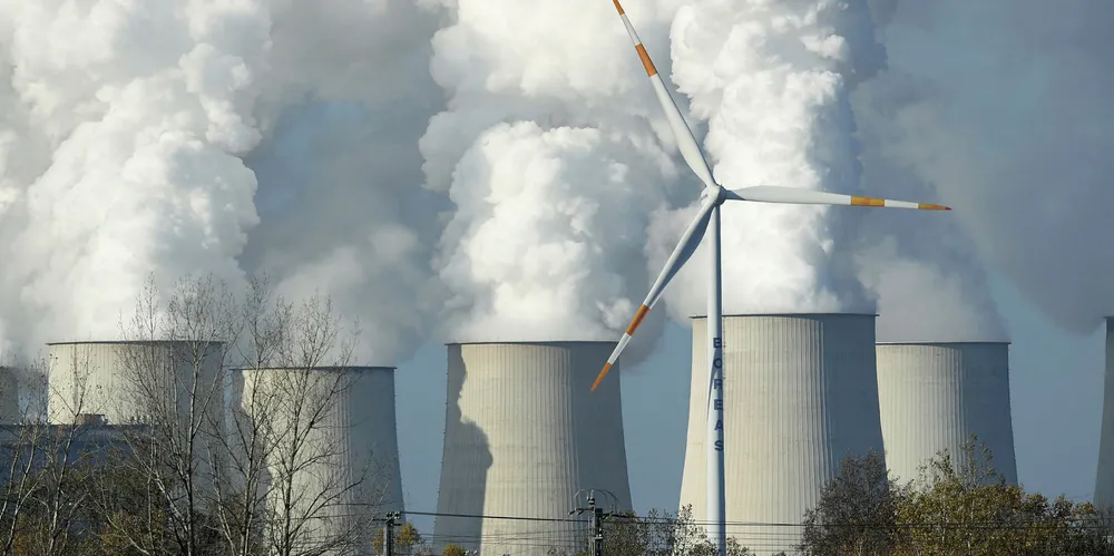A wind turbine spins as steam rises from the cooling towers of the Jaenschwalde coal-fired power plant in Germany