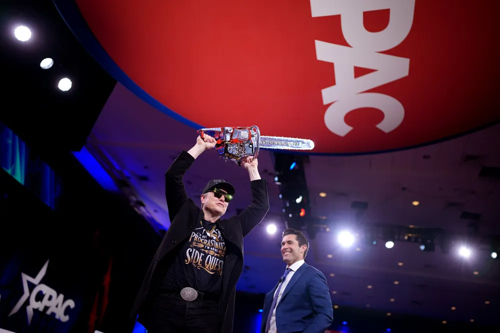 Elon Musk wields a chainsaw at a conference. The Tesla CEO has been leading Donald Trump's federal cost reduction drive.