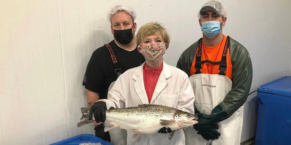 AquaBounty Processing Associates Skyler Miller (left) and Jacob Clawson (right), with CEO Sylvia Wulf (center) holding the first commercially harvested genetically modified farmed salmon in the United States. The company is decreasing its GM salmon production in Canada.