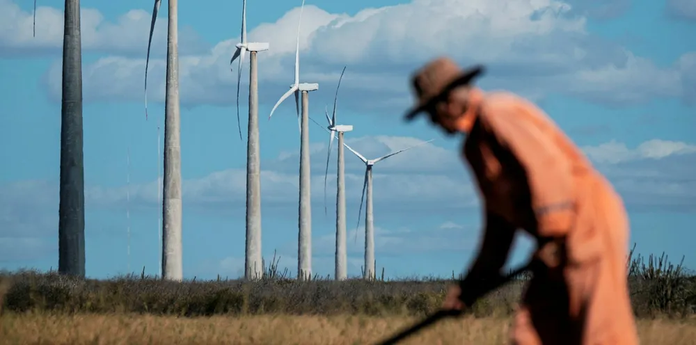 A farmer works near wind turbines at Vamcruz Windfarm, developed by three energy companies including French renewable energy power plants operator Voltalia Group, on June 29, 2016, in Serra do Mel, Rio Grande do Norte State, Brazil.