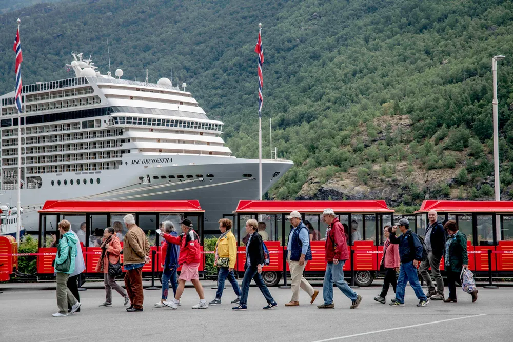 Cruiseturisme er stor business i Flåm. Her er en gruppe turister foran et cruiseskip og et turisttog i Flåm.
