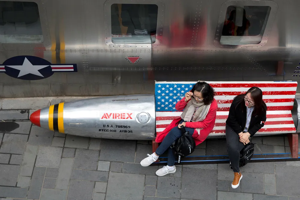 Kina protesterer mot USAs nye straffetoll. Her to kvinner på en benk med amerikansk flagg ved en amerikansk klesbutikk i Beijing. Foto: Ng Han Guan/AP/NTB Scanpix
