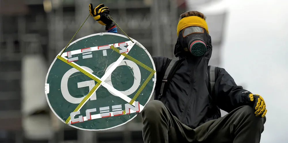A climate change protester wearing a gas mask and holding a STOP sign sits on the fence around the Houses of Parliament on October 15, 2019 in London, England.