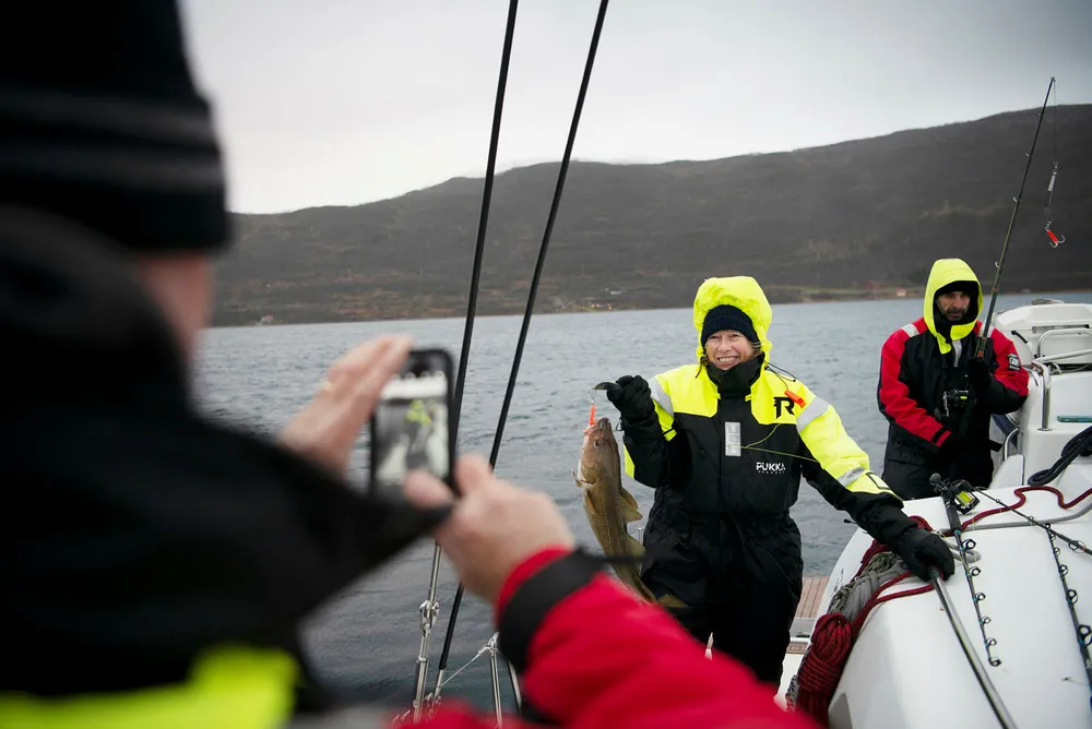 Steve Brown fra Texas tar bilde av kona Laura Brown, som akkurat har halt opp en torsk fra en av Pukka Travels seilkatamaraner i Kvalsundet nord for Tromsø. Turist Jose Galdon (til høyre) fikk ingen fisk.
