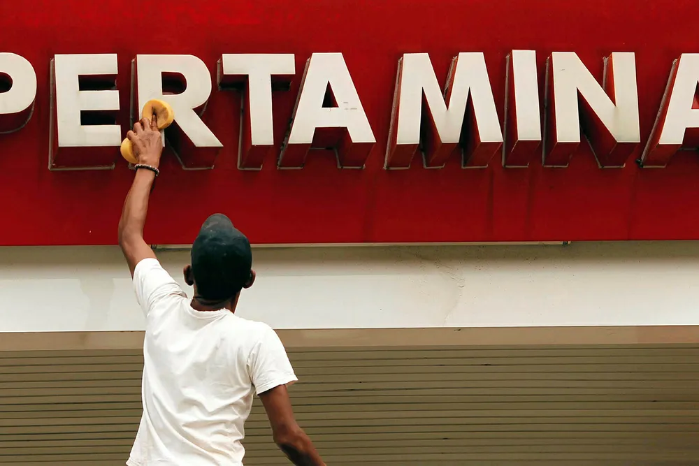 Operations: a worker cleans a sign of Indonesian state oil company Pertamina at a petrol station in Bekasi, Java