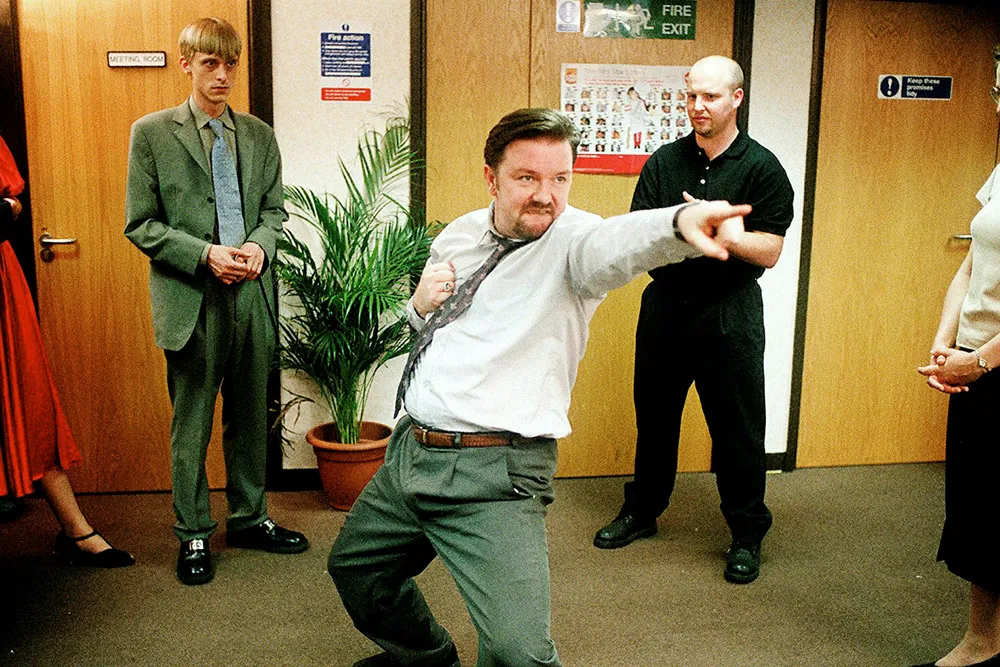 «The Office»-sjef David Brent spiller gjerne egenkomponerte låter på gitar for de ansatte. Foto: «The Office»