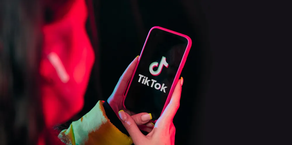 Vinnitsa,Ukraine - April 08, 2020.Tik tok advertisement concept. Young girl posing with smart phone in her hands,making selfie on black background.TIK TOK is a popular social network on the internet. . TikTok social media.