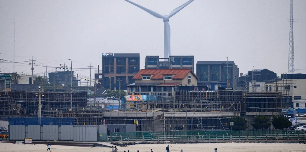 People walk before a construction site and a wind turbine on Woljeongri beach on Jeju island.