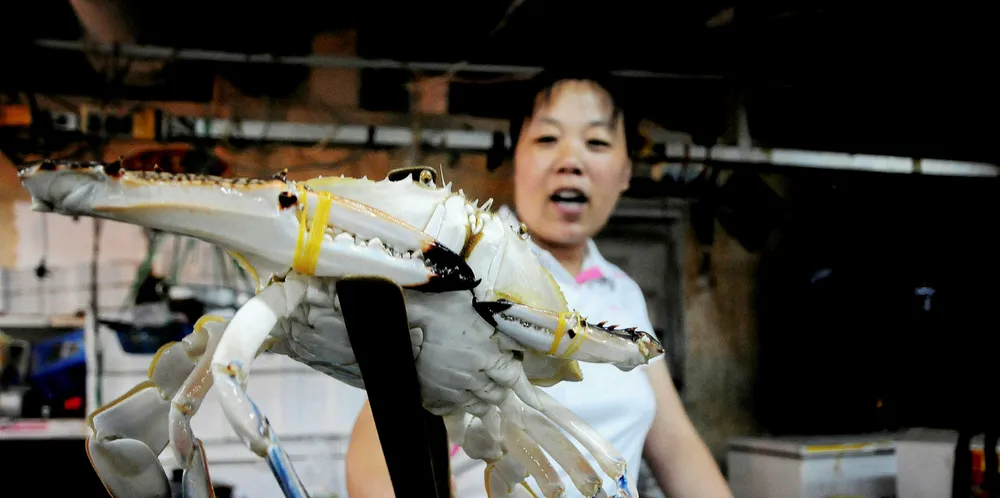 A vendor holds a crab as she waits for customers at a seafood market in Qingdao, in eastern China's Shandong province.