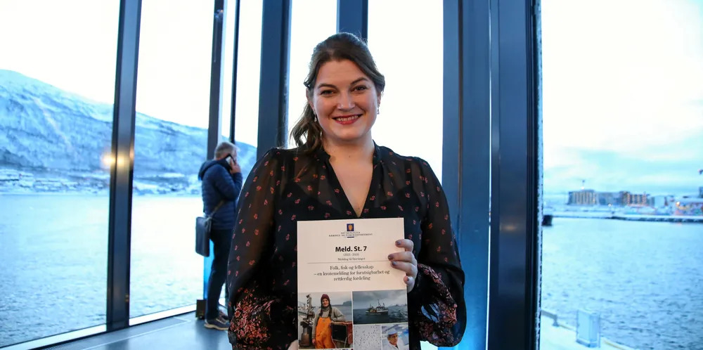 Fiskeristatsråd Cecilie Myrseth med kvotemeldingen i hånda. I bakgrunnen har Fiskebåts Audun Maråk sneket seg inn i bildet.
