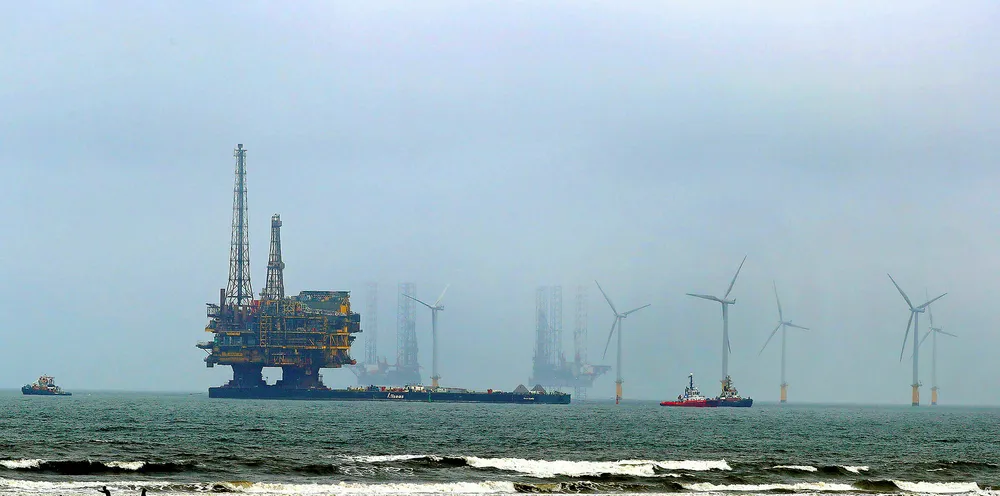 Shell's Brent Delta offshore oil platform is towed past wind turbines along the coastline of Hartlepool, UK