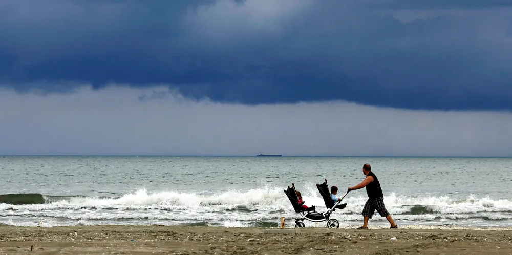 A man pushes a pram with two children on the Black Sea beach after a heavy rain in Navodari, Romania