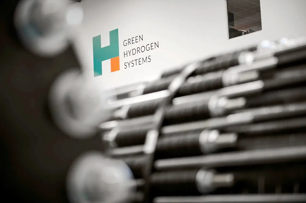 Green Hydrogen Systems' logo behind out-of-focus electrolyser stacks.