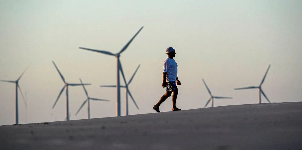 A man walk along the beach near wind turbines installed at Prainha do Canto Verde, in the Brazilian state of Ceara.