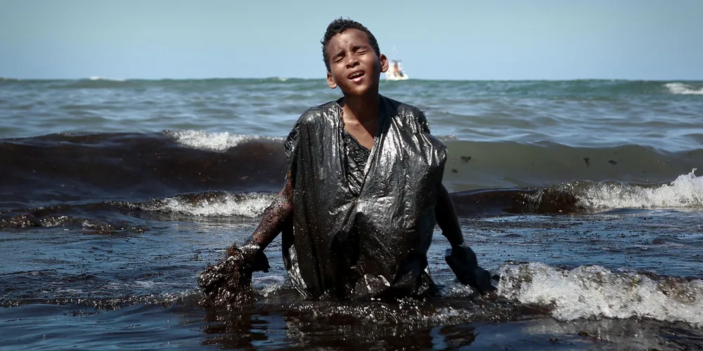 A boy walks out of the sea in October 2019 while removing oil spilt on Itapuama beach, in Cabo de Santo Agostinho, Brazil.