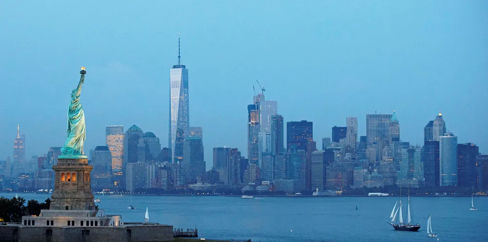 The Statue of Liberty stands in the foreground as Lower Manhattan is viewed at dusk.