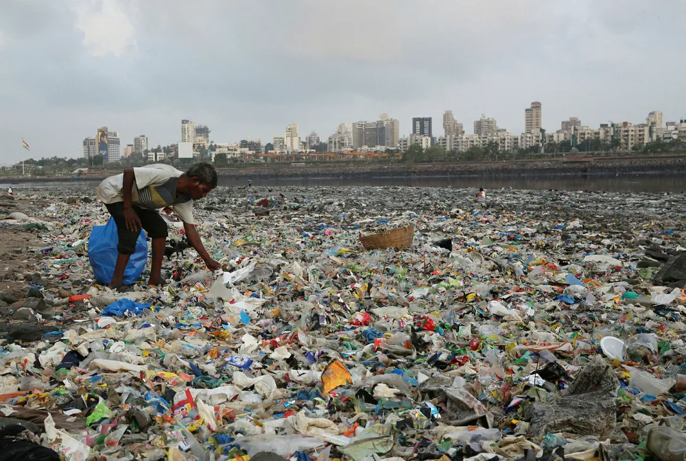 En mann samler inn plast og andre resirkulerbare materialer fra stranda langs Arabiahavet i Mumbai i India. Foto: Rafiq Maqbool/NTB Scanpix