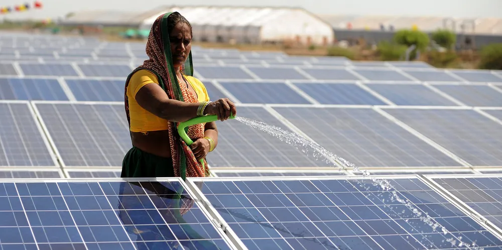 An Indian worker sprays water onto solar panels.