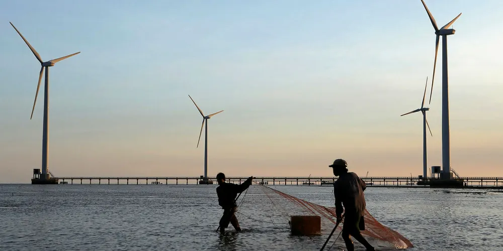Fishermen working near the first towers of wind turbines from Vietnam's first wind power plant along a sea coast on the southern coastal province of Bac Lieu.